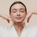 Mujer con ojos cerrados, manos en el mentón, disfrutando de los yoga facial beneficios.