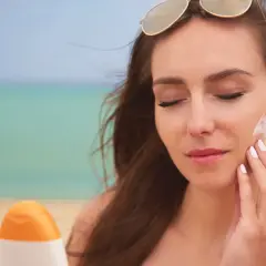 Mujer se aplica protector solar en la cara en la playa. El protector solar hidrata la piel mientras la protege del sol.
