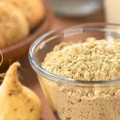 Maca en polvo en un bol de cristal, junto a raíces de maca. Se puede tomar ginseng y maca a la vez para potenciar sus beneficios.