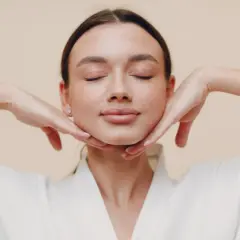 Mujer con ojos cerrados, manos en el mentón, disfrutando de los yoga facial beneficios.