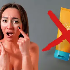 Mujer con piel enrojecida y expresión de sorpresa, señalando su mejilla. Un tubo de protector solar tachado con una X roja. Esto es lo que pasa si no te pones crema solar.