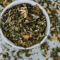 Taza blanca llena de hierbas secas y flores, un adaptógeno que es ideal para infusiones relajantes.