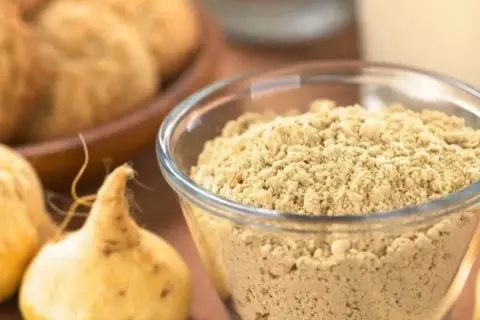 Maca en polvo en un bol de cristal, junto a raíces de maca. Se puede tomar ginseng y maca a la vez para potenciar sus beneficios.