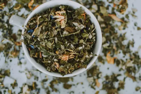 Taza blanca llena de hierbas secas y flores, un adaptógeno que es ideal para infusiones relajantes.