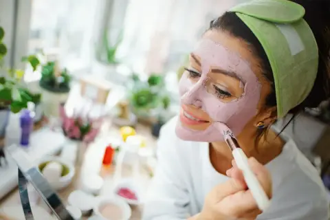 Mujer aplicándose mascarilla rosa, explorando los beneficios de los tipos de arcilla para la piel.