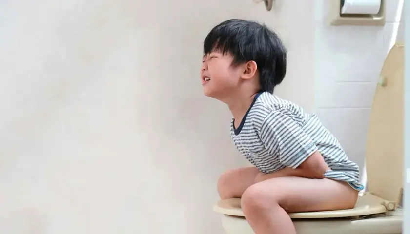 Niño de 5 a 10 años con estreñimiento, sentado en el inodoro con dolor y esfuerzo.