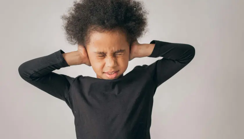 Niño con afro cubriéndose los oídos, mostrando malestar. Sugiere la necesidad de tratamiento para la ansiedad en niños de 5 a 12 años.