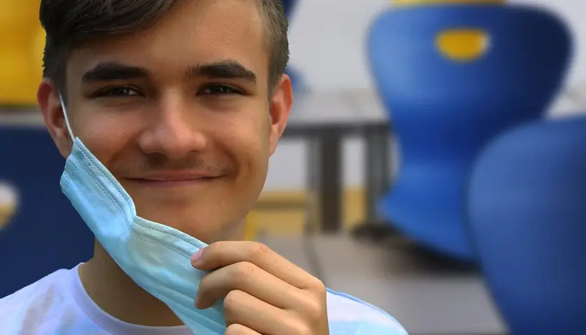 Joven sonriente se quita mascarilla, recordando la importancia de conocer los **covid en niños sintomas** para su bienestar.
