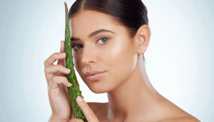 Una mujer joven con piel radiante sostiene una hoja de aloe vera, demostrando que el aloe vera es bueno para la cara.