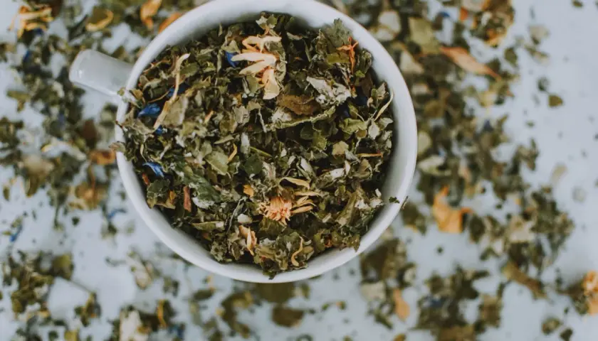 Taza blanca llena de hierbas secas y flores, un adaptógeno que es ideal para infusiones relajantes.