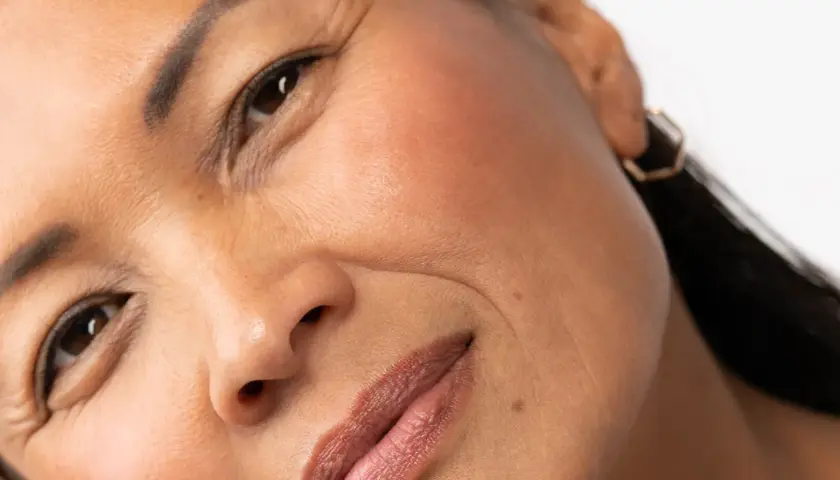 Primer plano de un rostro femenino, mostrando los signos de envejecimiento de la piel, como arrugas finas alrededor de los ojos y la boca.