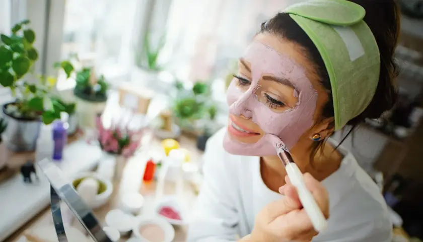 Mujer aplicándose mascarilla rosa, explorando los beneficios de los tipos de arcilla para la piel.