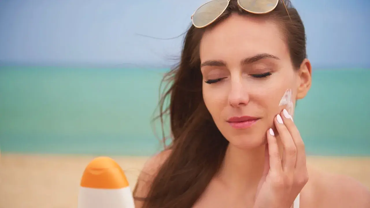 Mujer se aplica protector solar en la cara en la playa. El protector solar hidrata la piel mientras la protege del sol.