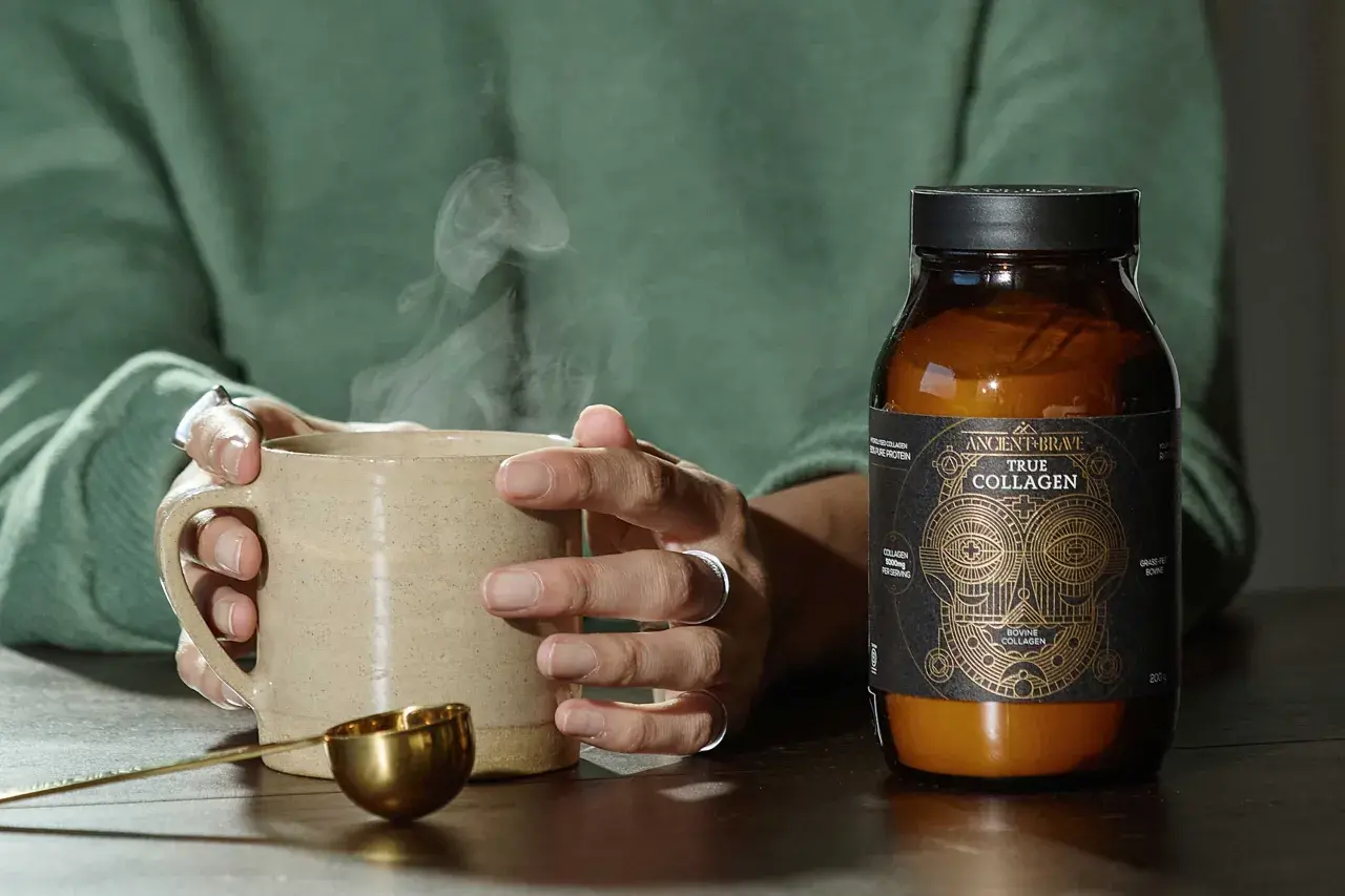 Manos sostienen taza humeante junto a un frasco de colágeno bovino, mostrando de qué está hecho el colágeno.