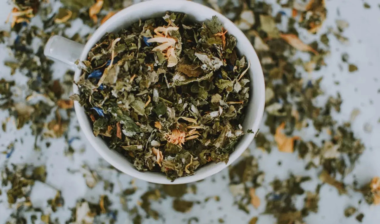 Taza blanca llena de hierbas secas y flores, un adaptógeno que es ideal para infusiones relajantes.