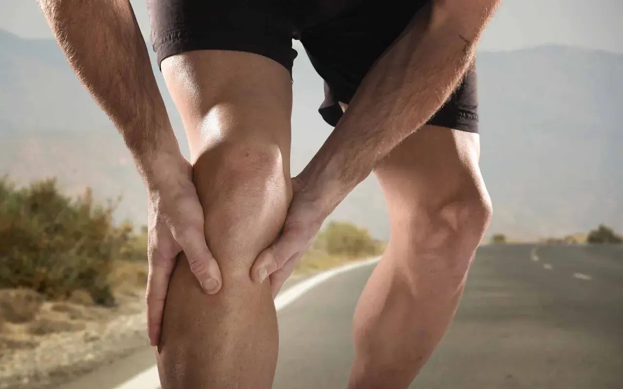 Un corredor sujeta su rodilla, sintiendo dolor. El dolor de rodillas en adolescentes deportistas es común.