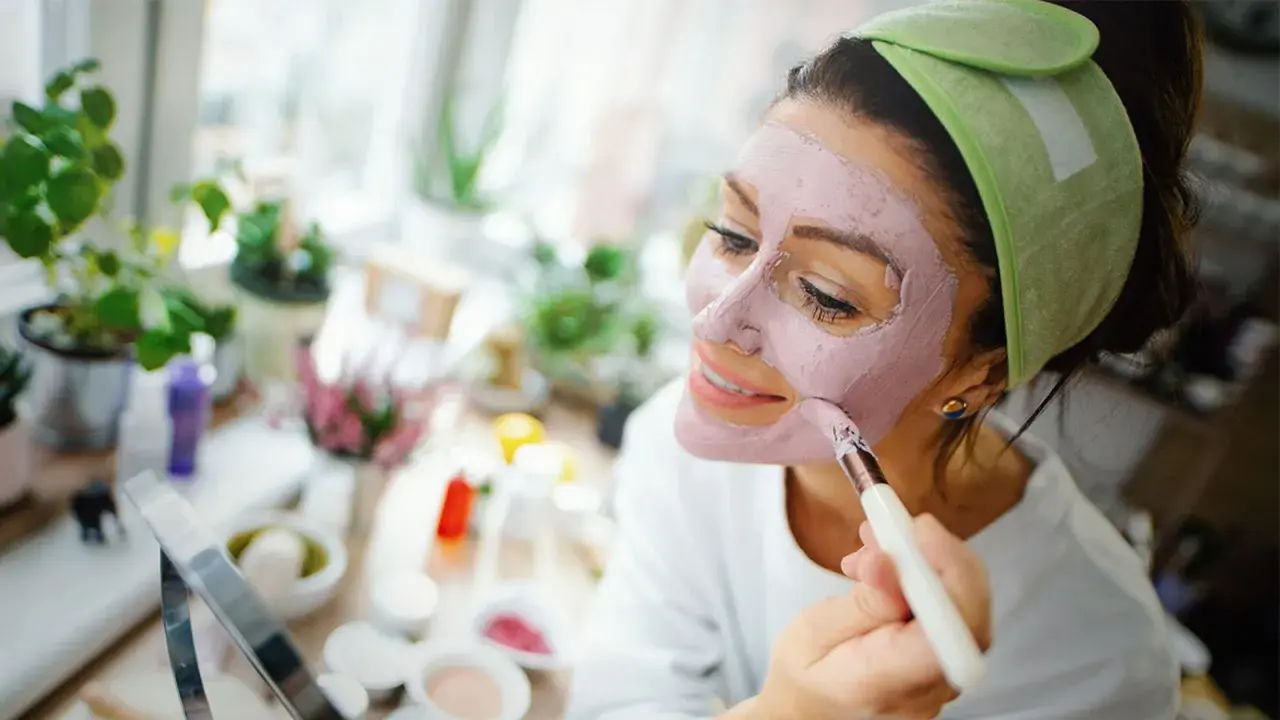 Mujer aplicándose mascarilla rosa, explorando los beneficios de los tipos de arcilla para la piel.