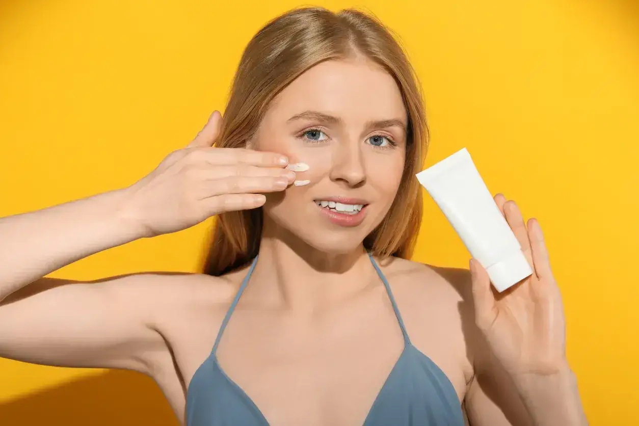 Una mujer rubia aplica crema solar en su rostro, mostrando para qué sirve el protector solar en la cara: protegerla del sol.